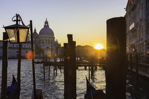Romantic Italian city of Venice in sunset. World Heritage Site. Traditional Venetian wooden boats, gondolier and Roman Catholic church Basilica di Santa Maria della Salute.
