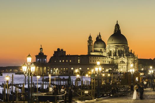 Romantic Italian city of Venice in sunset. World Heritage Site. Traditional Venetian wooden boats, gondolier and Roman Catholic church Basilica di Santa Maria della Salute.