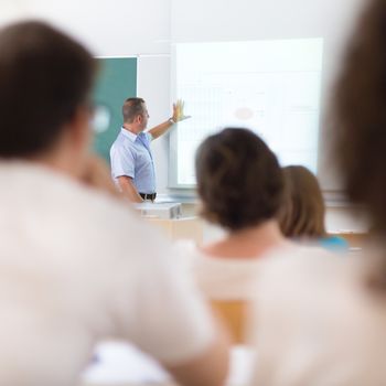 Teacher at university in front of a whiteboard screen. Students listening to lecture and making notes.