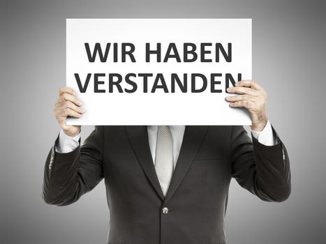 A business man holding a paper in front of his face with the message we understood in german language