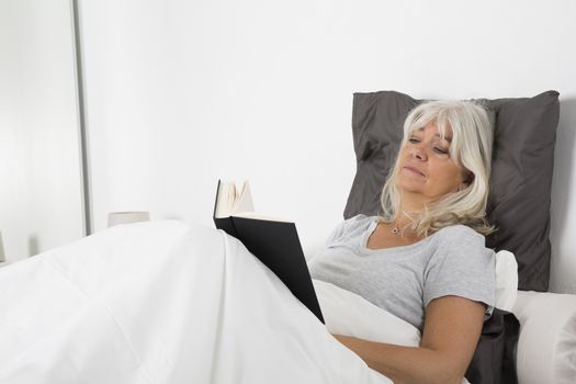 Tired woman reading a book in bed
