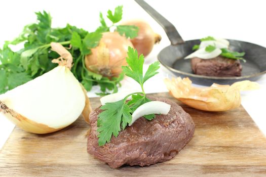 Ostrich steak with onions and parsley on a light background