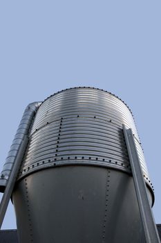 large stainless steel grain silo against a clear blue sky background