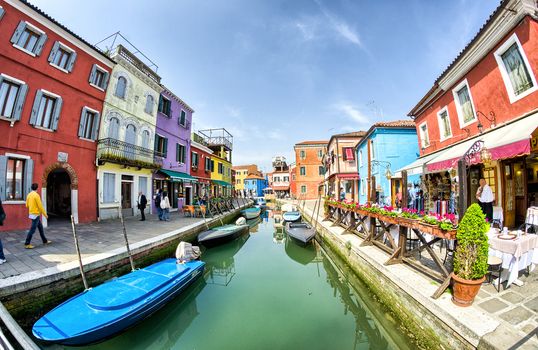 BURANO, ITALY - APRIL 8, 2014: Tourists enjoy colourful city buildings on a beautiful spring day. Island Burano village colors attract one million tourists annually.