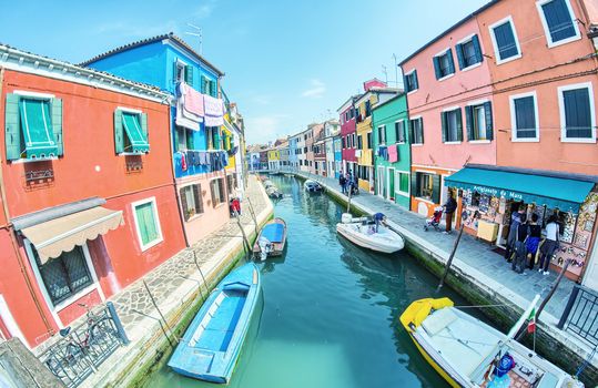 BURANO, ITALY - APRIL 8, 2014: Tourists enjoy colourful city buildings on a beautiful spring day. Island Burano village colors attract one million tourists annually.
