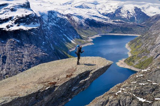 Hiker with backpack on Trolltunga rock high above scenic fjord in Norway