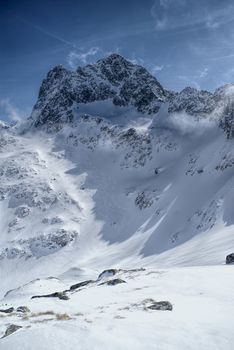 Breathtaking over of rocky peaks hidden in the shadow with sun shining over snowy slopes