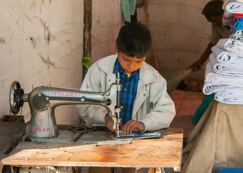 NAGAUR, INDIA - CIRCA FEBRUARY 2011: Child labor, boy sewing in booth on the market.