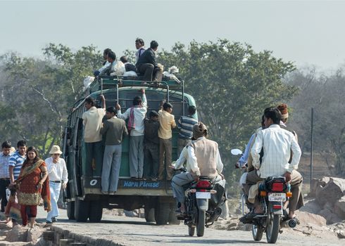 ORCHHA, INDIA - CIRCA FEBRUARY 2011 - Overloaded public transport bus carrying people on top and hanging out at the back.