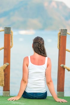 Brunette sits on the edge of the pier in the evening