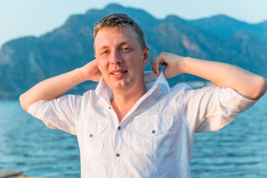 man straightens his shirt collar near the sea