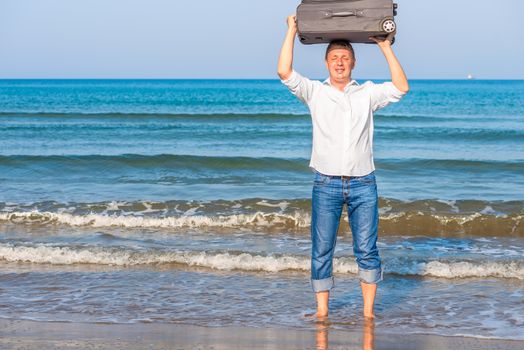 happy man with suitcase barefoot in the sea