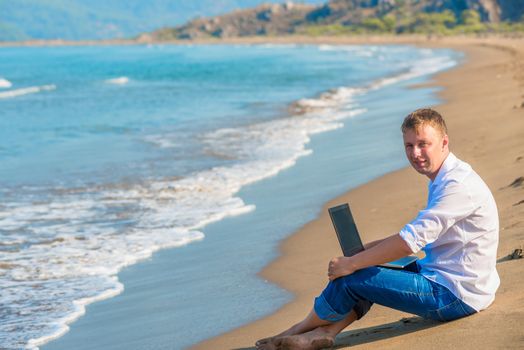 smiling man sitting on the sand beside the sea