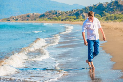 man in jeans and a white shirt walking along the seashore