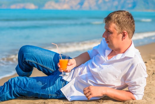 a man lies with a cocktail on the sandy beach in clothes