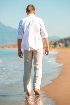 male in white clothing walking along the beach