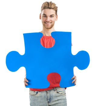 Good looking young man holding a blue puzzle piece, isolated on a white background