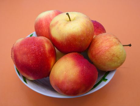 Red and yellow apples with kalyami water on their surface in the plate on an orange background