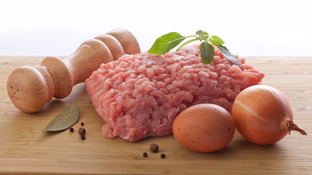 Minced meat with green basil, bay leaf, black pepper, egg and onion on the wooden board