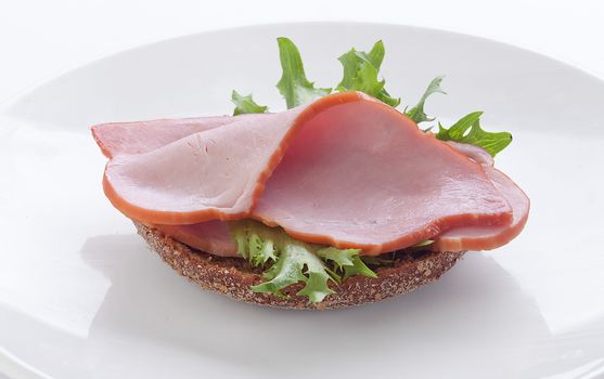 Sandwich with rye bread, pork loin and fresh green lettuce on the white plate