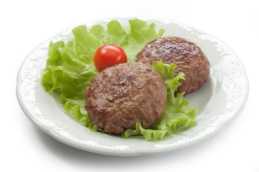 Two meat rissoles with fresn green lettuce and tomato cherry on the white plate