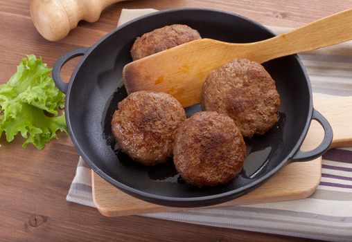Meat rissoles in the iron pan with green lettuce on the wooden table