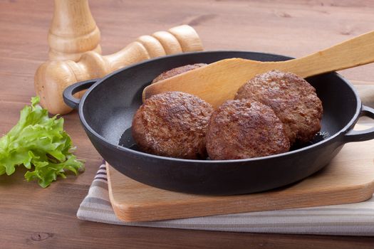 Meat rissoles in the iron pan with green lettuce on the wooden table