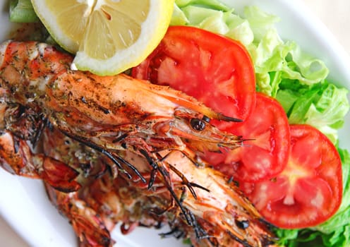 Fresh grilled shrimps with tomatoes, green salad and lemon on white plate 