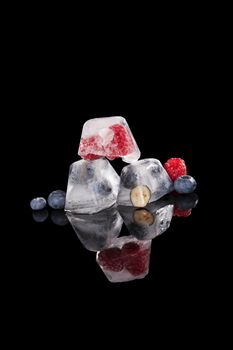 Blueberries and raspberries frozen in ice cubes black background. Fresh fruit eating. 