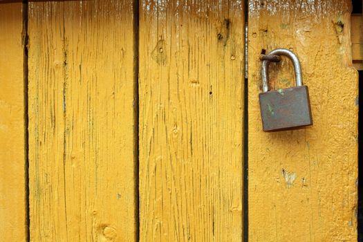 old metallic padlock on yellow wooden door, interesting textured view