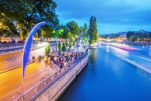 PARIS - JUNE 13, 2014: Tourists along Seine river at dusk. More than 30 million people visit the city every year.