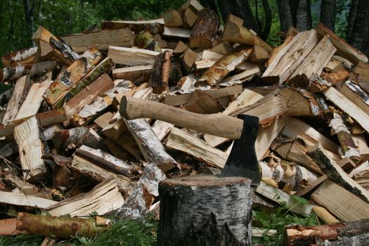 The axe on the background of a pile of wood in green forest