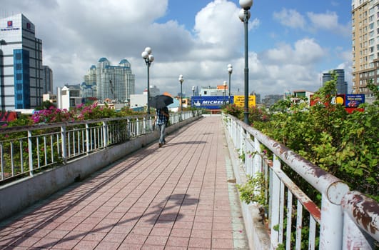 HO CHI MINH CITY, VIETNAM- JULY 3: Young man walking on overpass with umbrella in hand in hot day, he walk alone, cloudy sky, sunshine in summer, Viet Nam, July 3, 2014 