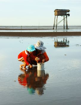 MEKONG DELTA, VIETNAM- JULY 8: Unidentified Vietnamese children, mother reflect on surface water of black sand sea, they earn money by catch shell fish before leaf watch tower , Viet Nam, July 8, 2014