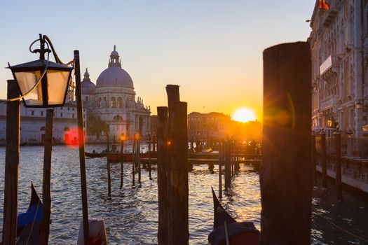 Romantic Italian city of Venice in sunset. World Heritage Site. Traditional Venetian wooden boats, gondolier and Roman Catholic church Basilica di Santa Maria della Salute.