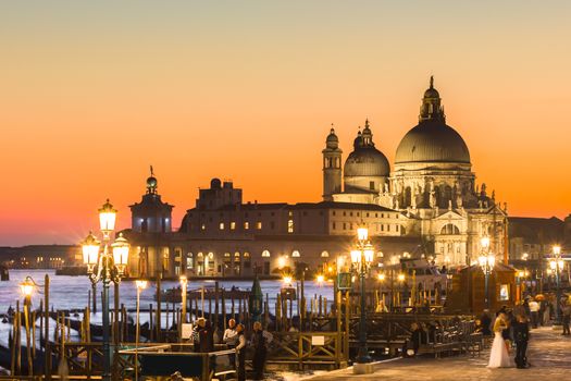 Romantic Italian city of Venice in sunset. World Heritage Site. Traditional Venetian wooden boats, gondolier and Roman Catholic church Basilica di Santa Maria della Salute.
