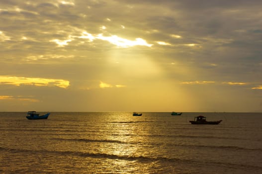 Silhouette of group of fishing boat on sea, seascape at sunrise, sky with cloud, sun ray shine on water make beautiful landscape