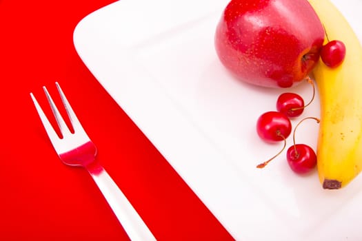 A white plate with fruit on red background.
