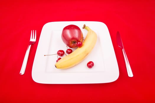 A white plate with fruit on red background.
