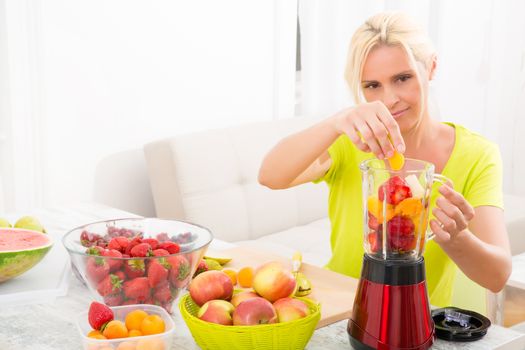 A beautiful mature woman preparing a smoothie or juice with fruits in the kitchen.
