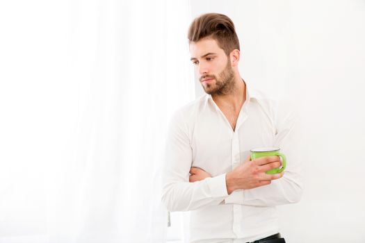 A young adult man at home drinking coffee.
