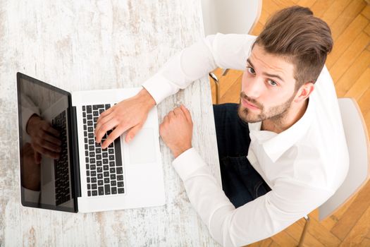 A young man sitting at the table with a laptop computer.