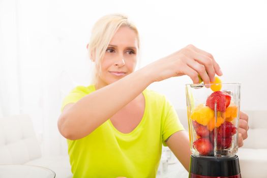 A beautiful mature woman preparing a smoothie or juice with fruits in the kitchen.
