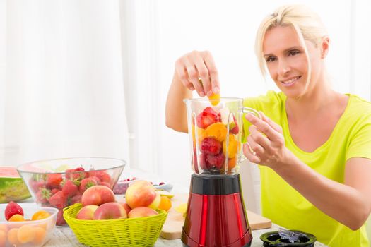 A beautiful mature woman preparing a smoothie or juice with fruits in the kitchen.
