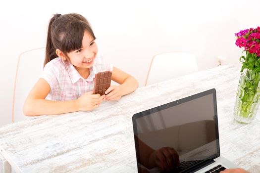 The daughter eating chocolate while her mother is working on a Laptop computer.