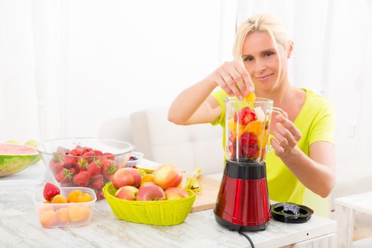 A beautiful mature woman preparing a smoothie or juice with fruits in the kitchen.
