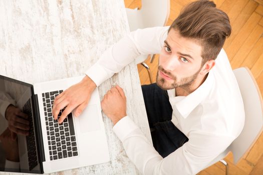 A young man sitting at the table with a laptop computer.