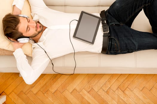 A young handsome man on the couch listening to music.
