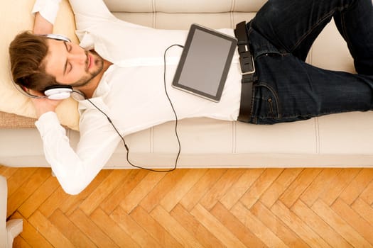 A young handsome man on the couch listening to music.
