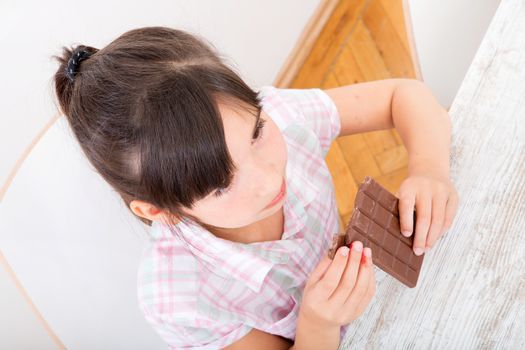 Girl eating chocolate at the table at home while the mother is working.
